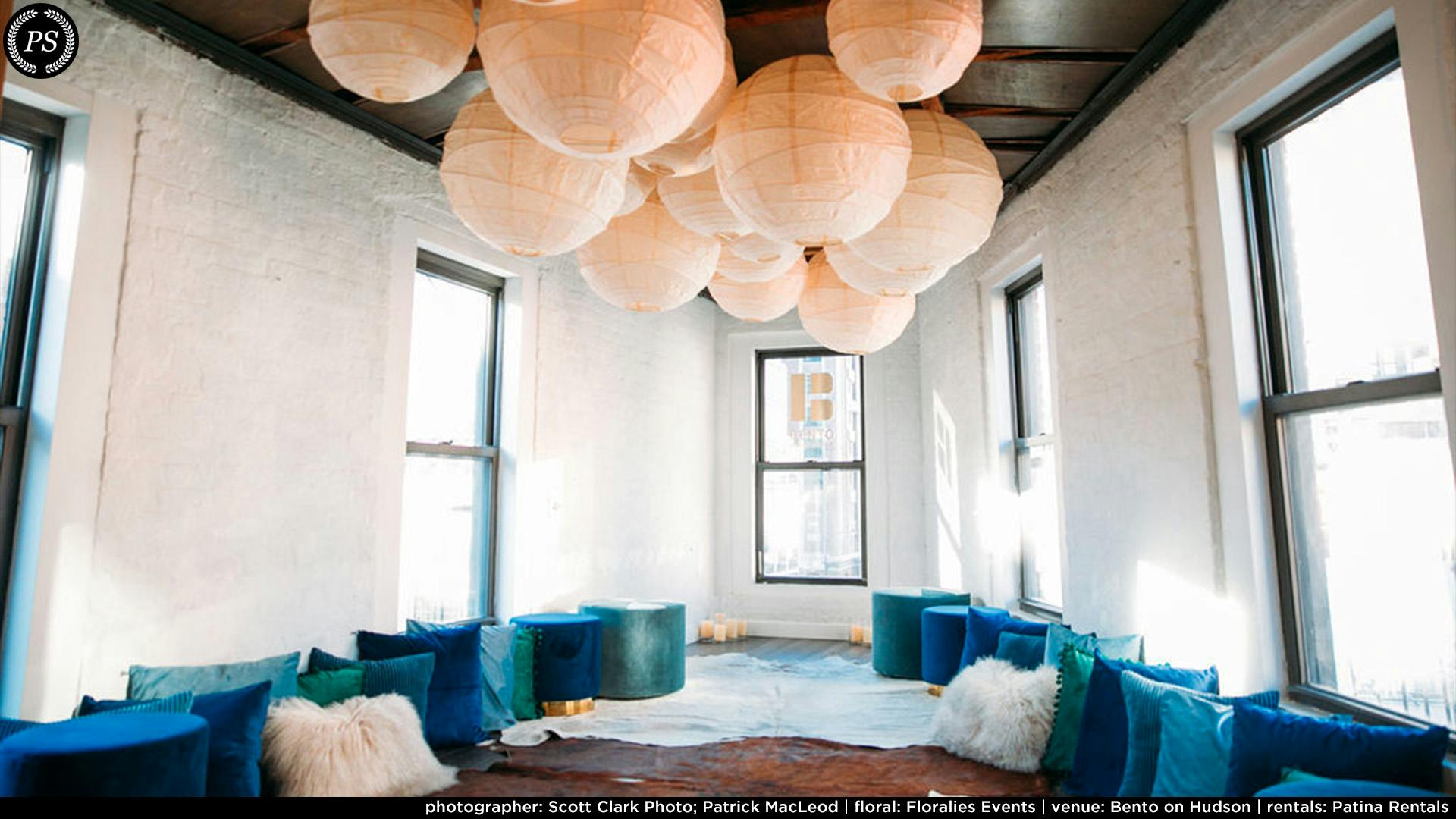A white walled loft with Chinese lanterns on the ceiling and blue poufs on the floor