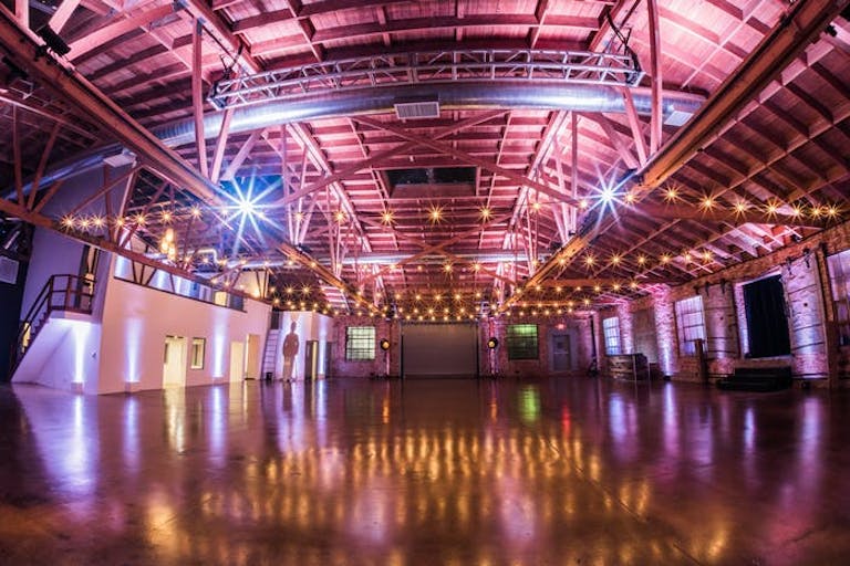A massive warehouse with a vaulted ceiling and pink and purple lighting everywhere