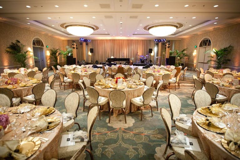 Round cream tables are in a ballroom with two lights coming from the ceiling next to recessed lighting.
