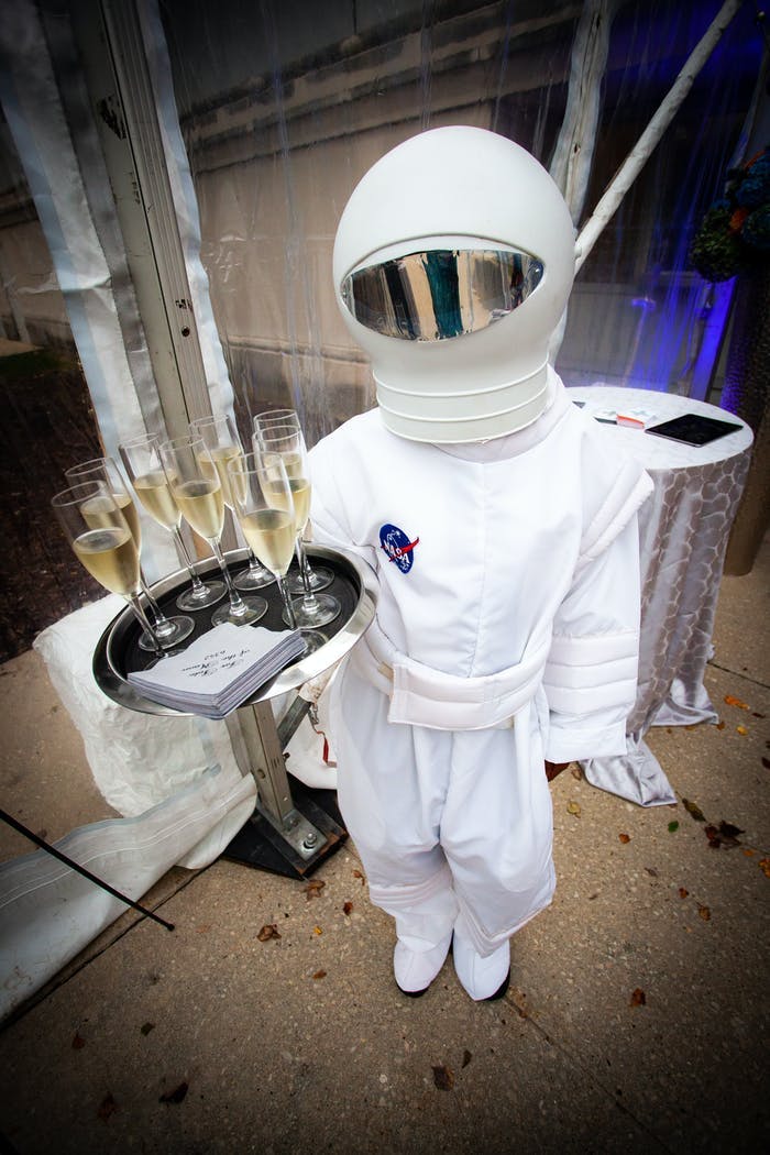 Space-Themed Party With Person in a Space Costume Holding a Tray of Champagne