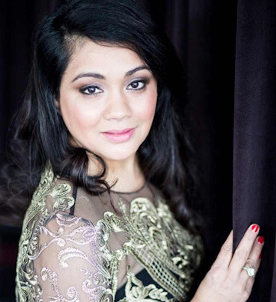 A headshot of Sonal J Shah. A black background and she stands with her hand on the wall in front of her.