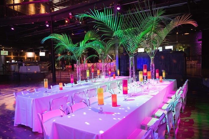 two long tables with white linens and palm leaves acting as center pieces