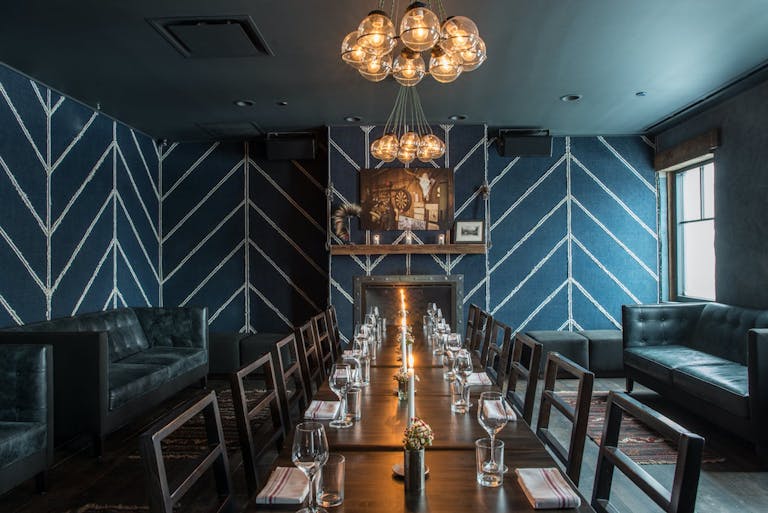 Private dining space with blue and white triangle-patterned walls, globed lighting, and a wooden banquet table.