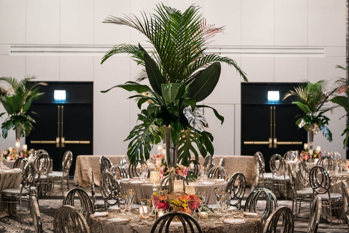A ballroom with white walls and round tables and tall greenery as the centerpieces