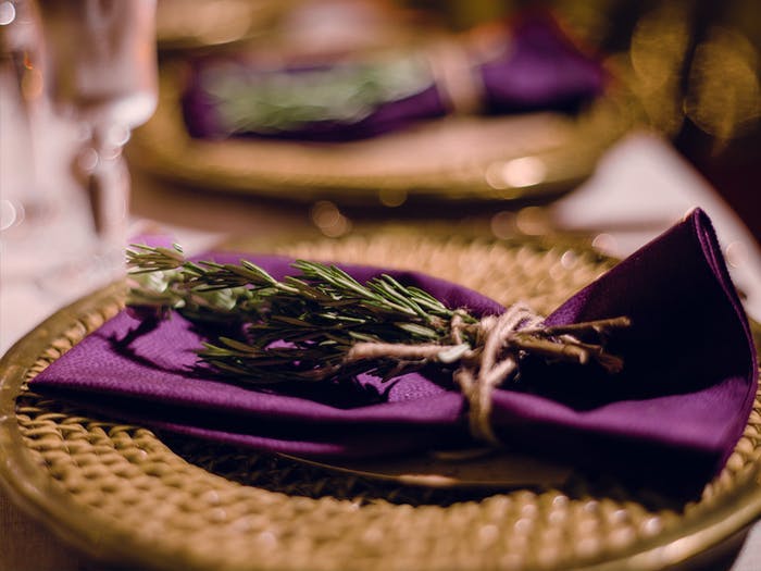a wicker charger with purple napkin on top with sage layed on it