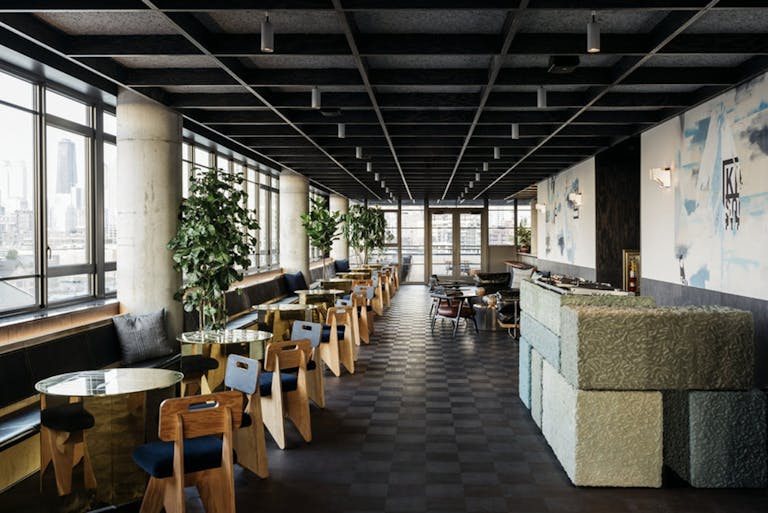 Indoor rooftop bar with floor to ceiling windows on left side of photo.