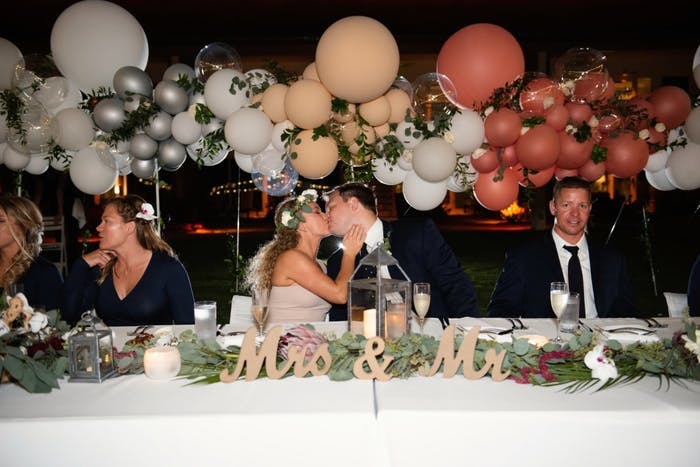 A couple kissing at their head table with multicolored balloons behind them
