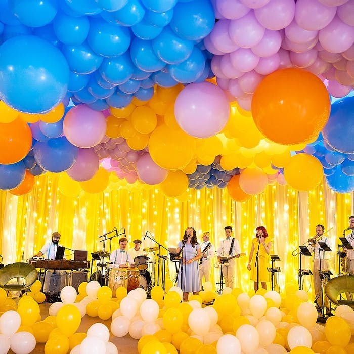 A stage covered in yellow balloons and yellow tinsel with blue and pink balloons covering the ceiling