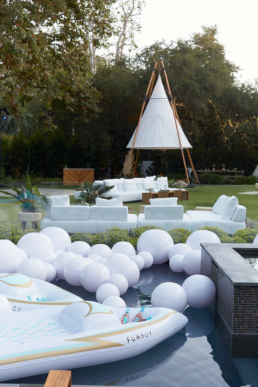 a pool with white balloons floating on top. In the background is a white tent with couches