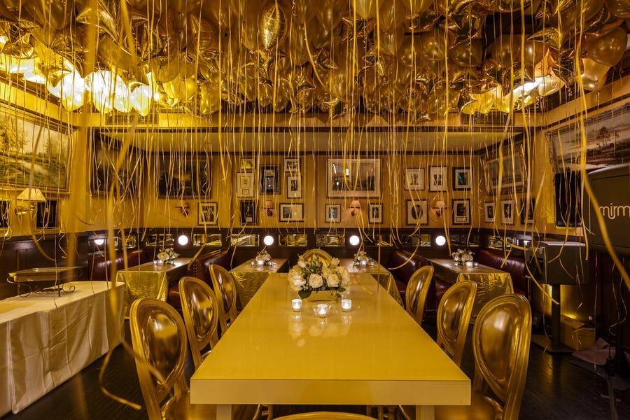 looking down the length of a long table. A wash of yellow/orange light and balloons with long ribbons hanging down