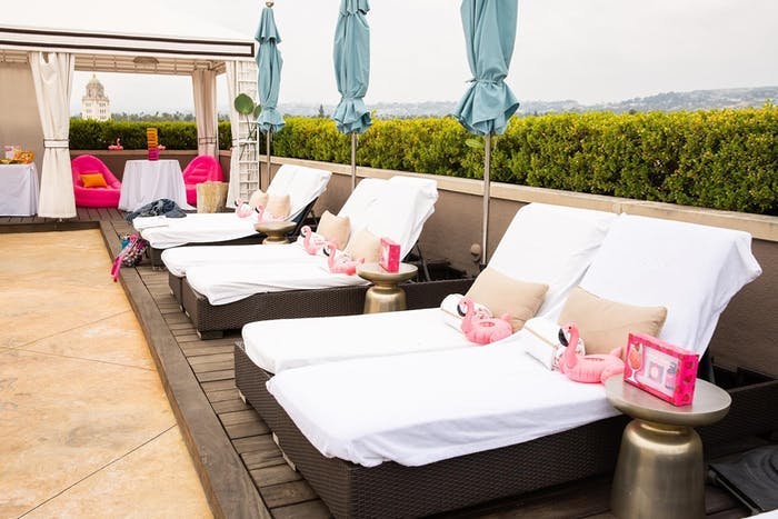 A rooftop patio looking over the landscape. White lounge chairs and pink pillows line the wall
