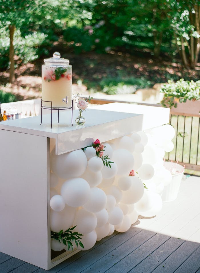 an agua fresca station with white balloons clustered underneath