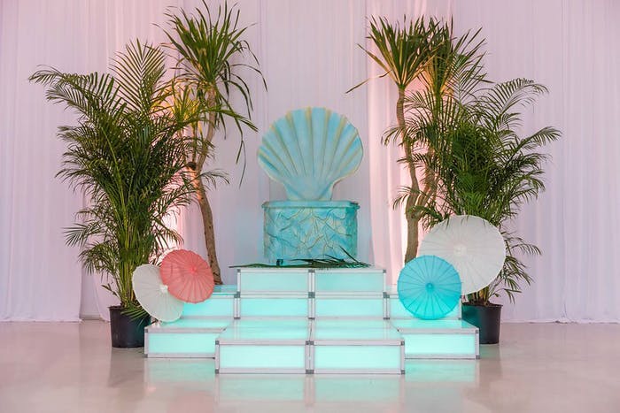 A throne style seat made to look like a giant sea shell with blue footstools in front. Leaves sit on either side of this.