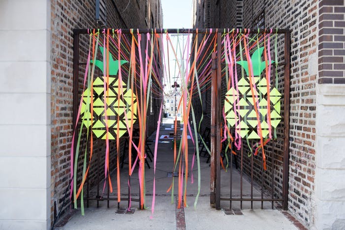 An alley way with streamers hanging from the gates and pineapple pinned