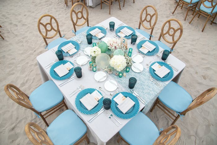 An above view of a square tablescape with a white linen and blue place settings.