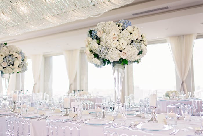 An all white tablescape with a tall floral arrangement and transparent seating