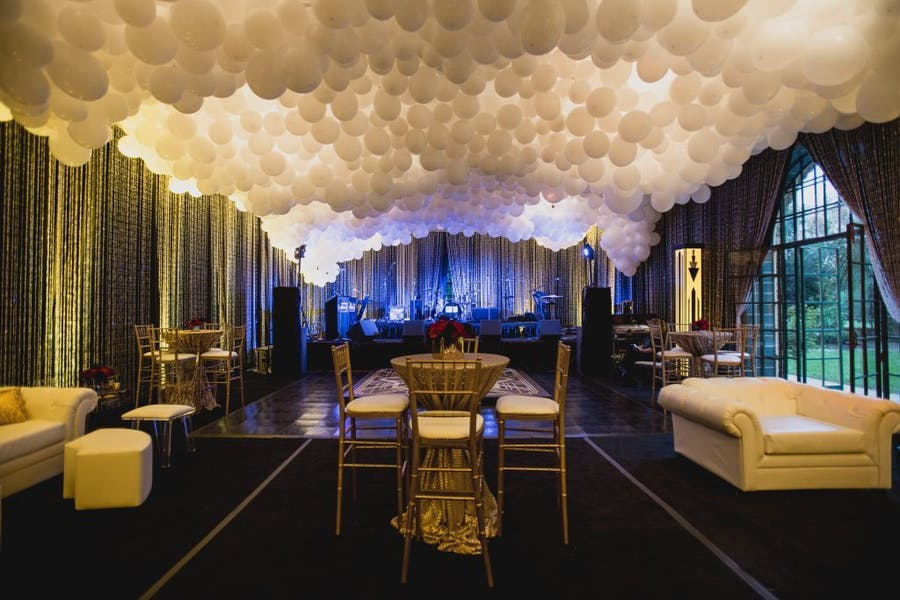 A long room with a stage lit blue at the end. White balloons cover the ceiling