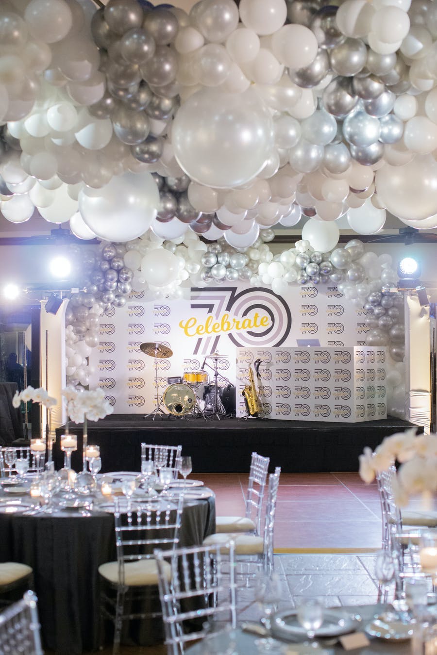 A room looking at a stage with instruments on it. White and silver balloons over the ceiling