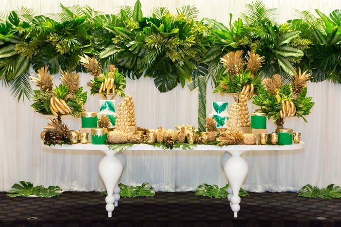 A decor table with greenery hanging above and all accessories painted gold