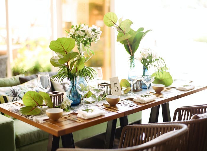 An earth toned photo with a small wooden table with place settings. Green leaves make up the centerpiece
