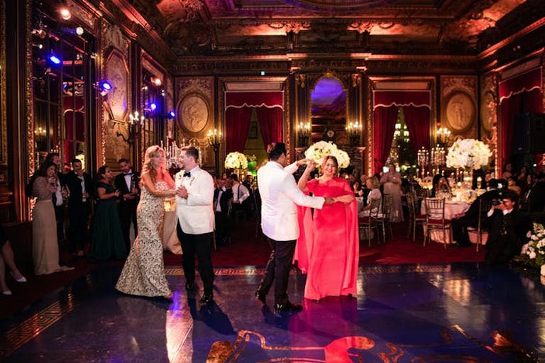 2 couples dance on the dance floor. The men wear white jackets and the lighting is warm.