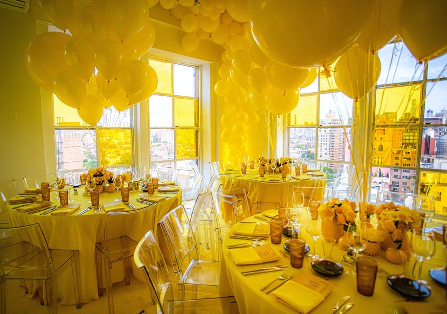 A corner with windows on both sides. Yellow balloons in the center of each table and a glow of yellow throughout the whole room