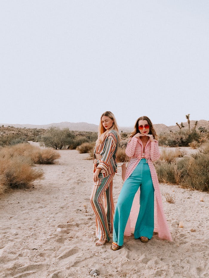 Two young women standing in the sand wearing 70s outfits | PartySlate