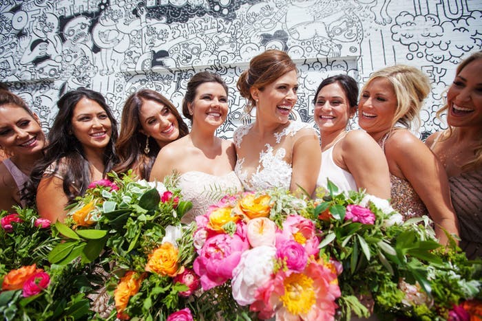 a bridal party stands in front of a black and white wall with colorful peonies and greenery