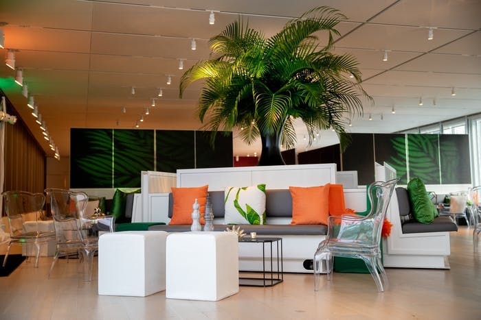 A room with white furniture and orange pillows. A palm tree is in the middle of the room