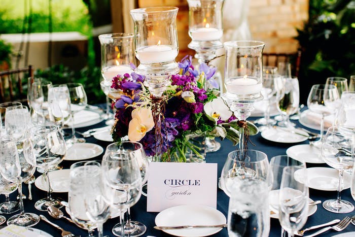 purple flowers in the center of the table with glassware and candles surrounding.
