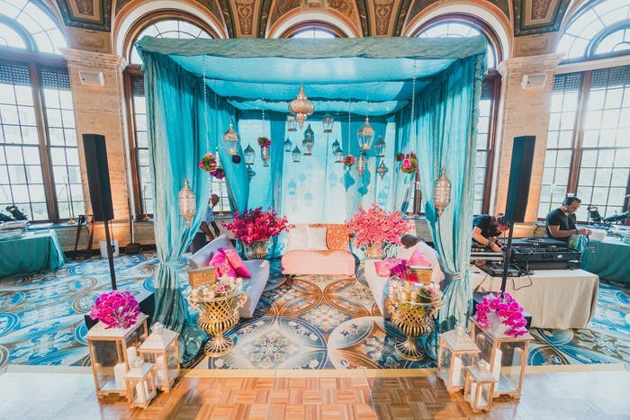 A blue backdrop with pink floral arrangements. Large windows on either side