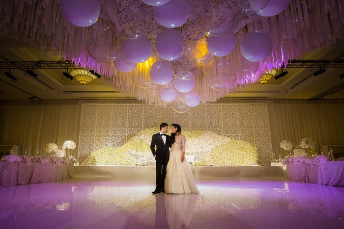 A couple standing on a dance floor. Purple and yellow lighting washes over the,,