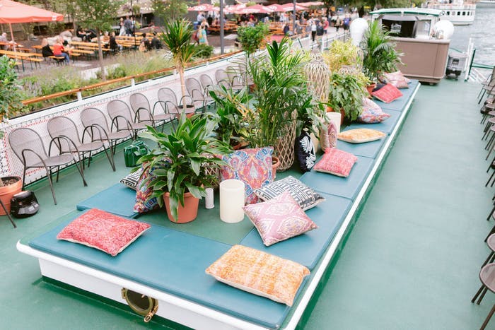 A boat deck with a communal seating area in the center. Colorful pillows mark each seat and ferns are in the center. Chairs go along the outside of the deck