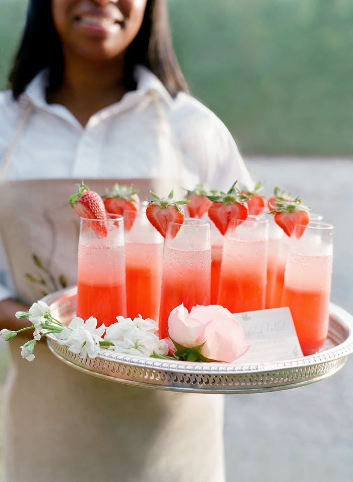 Woman holds a tray of red drinks with strawberries as garnish