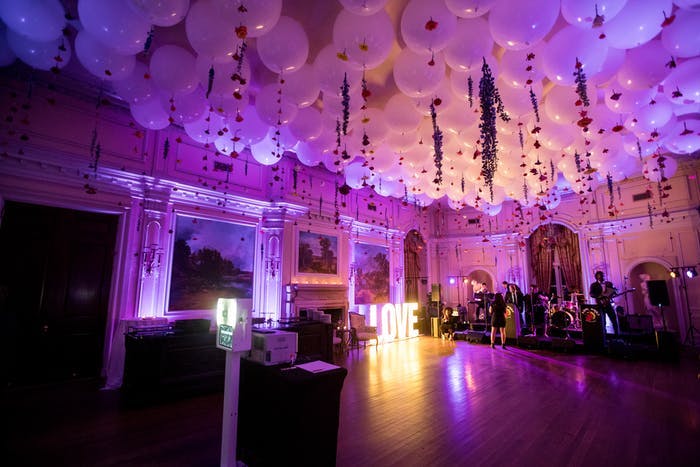 A large balroom dance floor lit up purple with white balloons covering the cieling