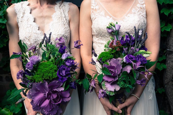 Two brides in white dresses holding purple and green bouquets