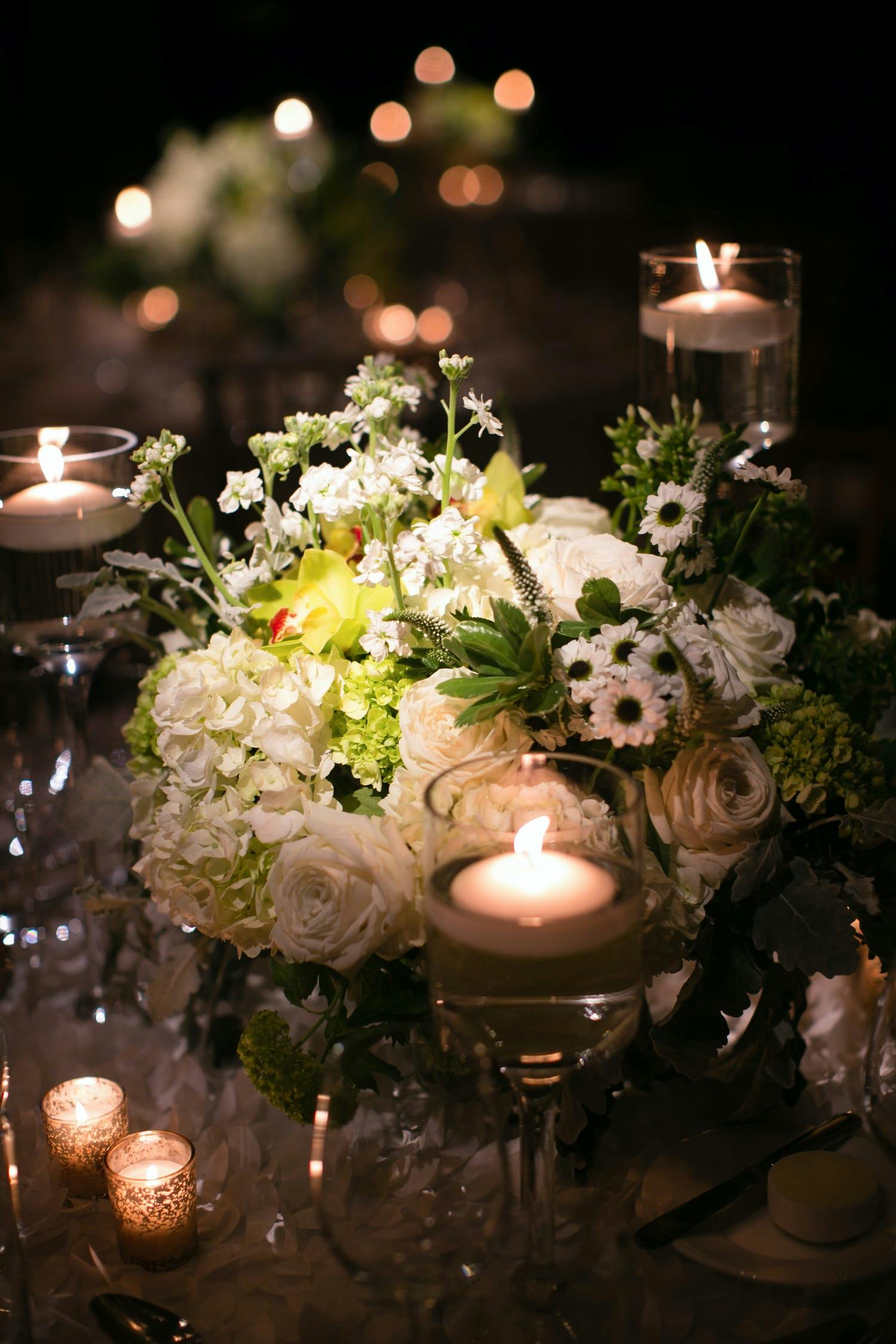 Close up of white hydrangea centerpiece with yellow-green accent blooms and an accompanying candlelight.