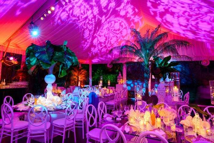 A tented room with a wash of pink lighting. Palm trees act as centerpieces and glowing candles surround them