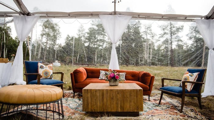 Burnt orange couch and chairs under a white linen canopy in a wooded area