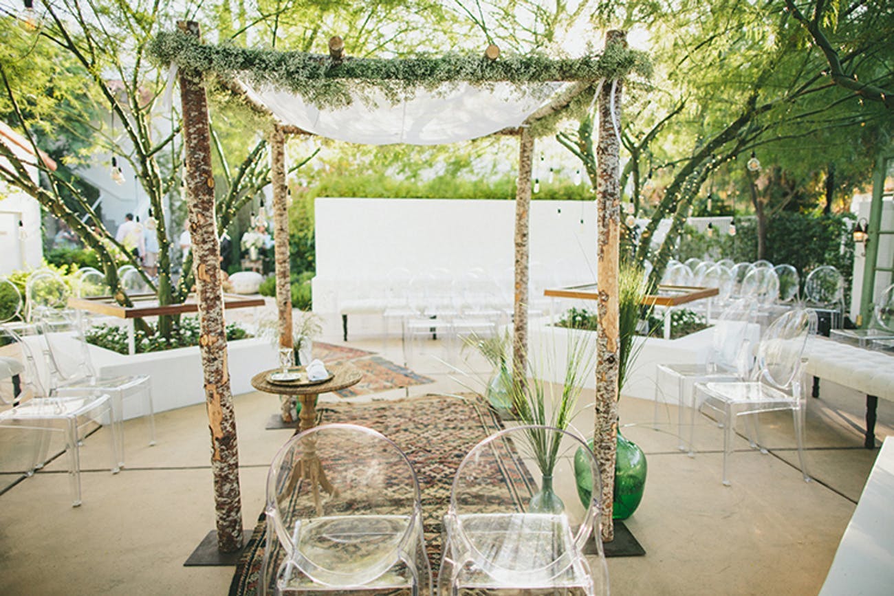 Outdoor wedding ceremony with lucite seating and rustic arch.
