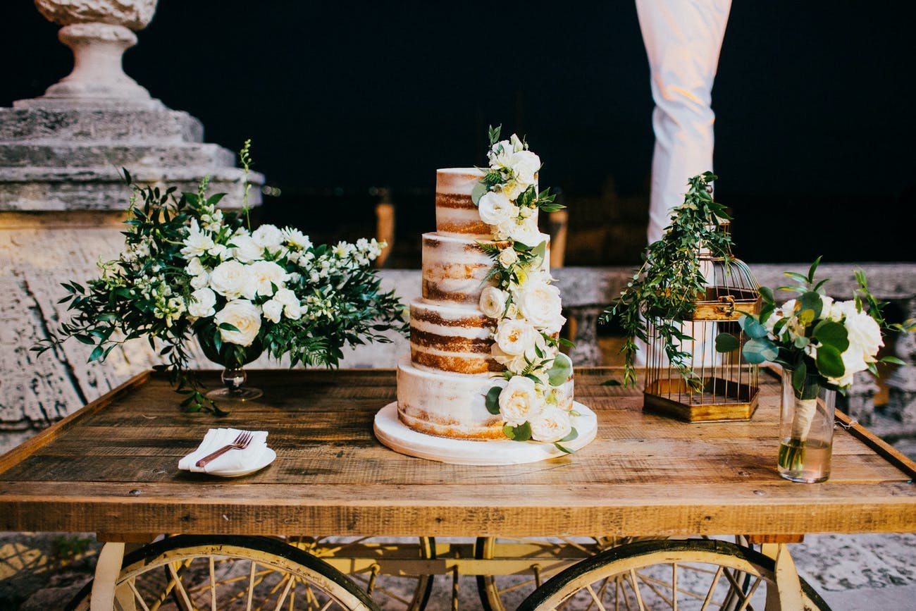 Gold and white wedding cake displayed on rustic bar cart.