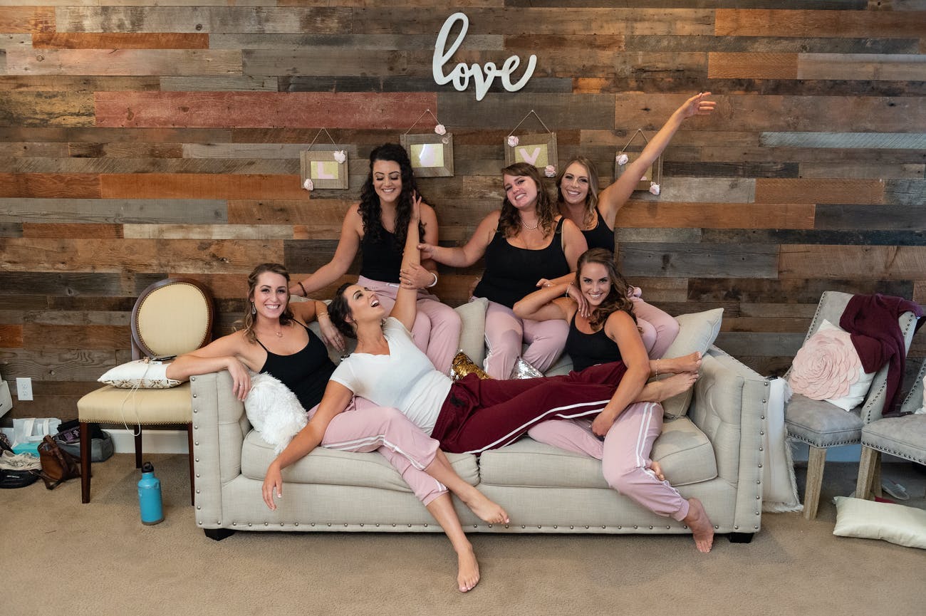 Bridal party poses on a sofa in front of a wooden wall and rustic wedding sign that reads 