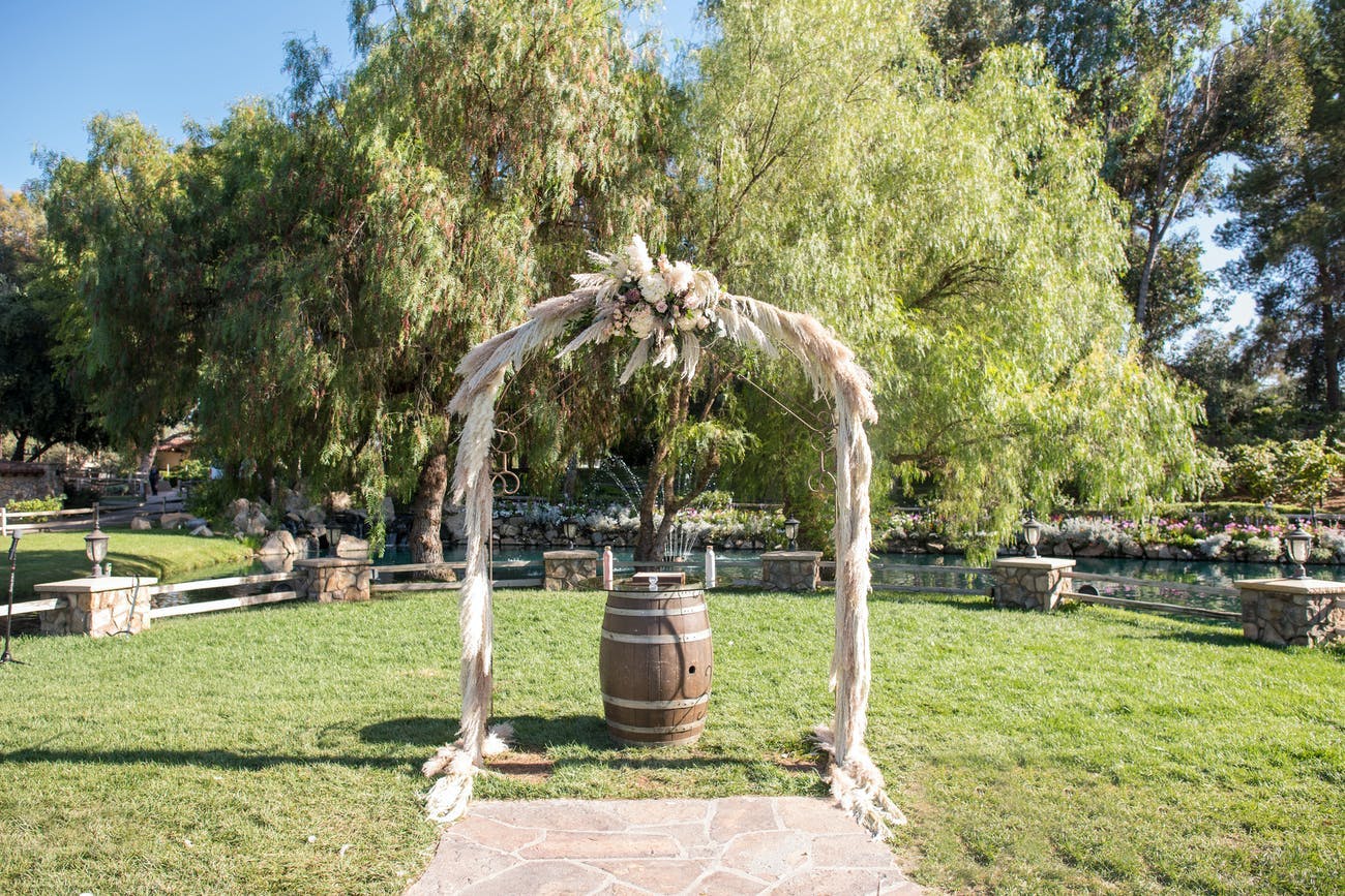 Rustic wedding arch with pampas grass and a rustic wine barrel.