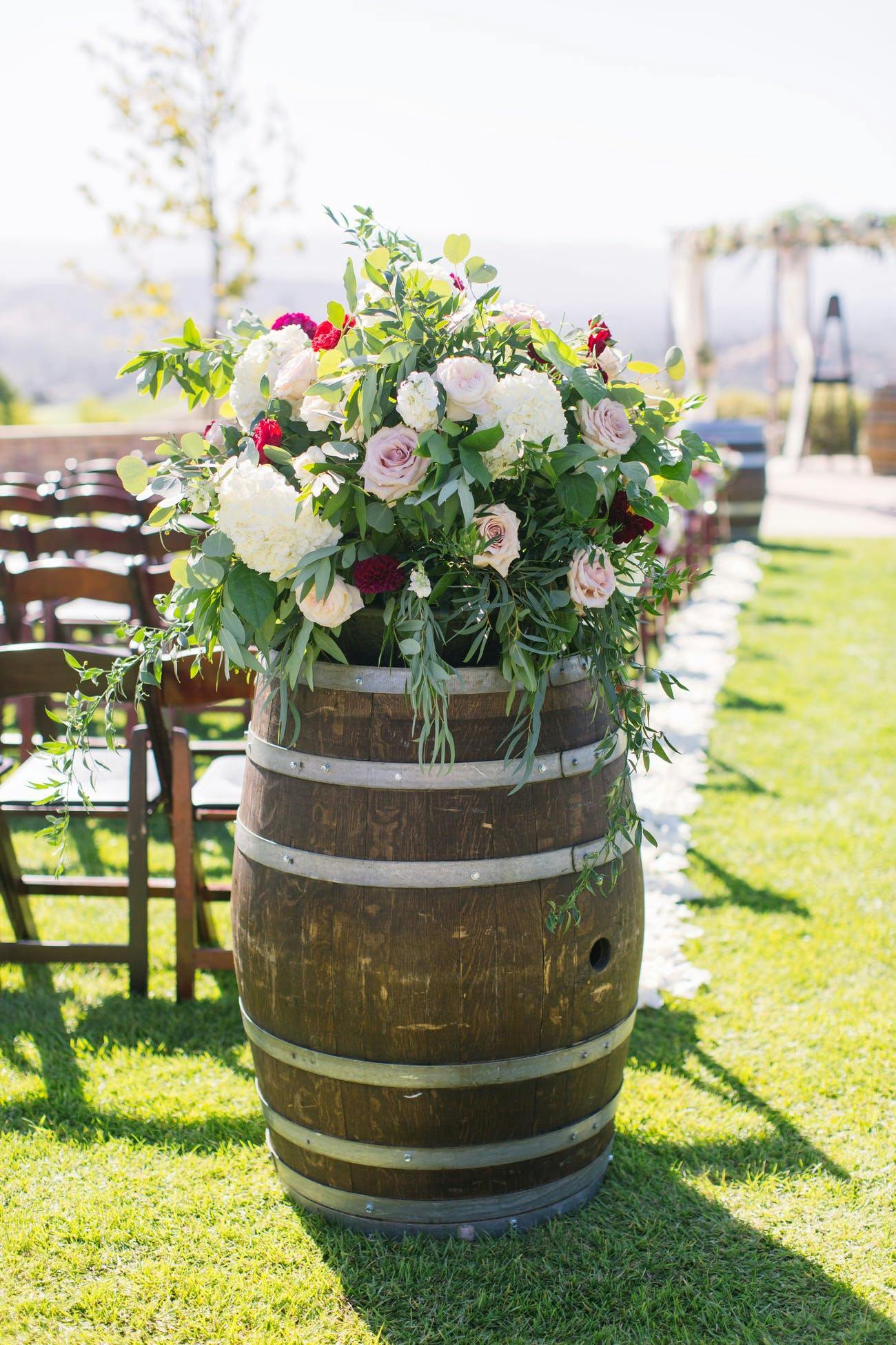 Rustic wedding aisle décor featuring a vintage wine barrel with flowers.