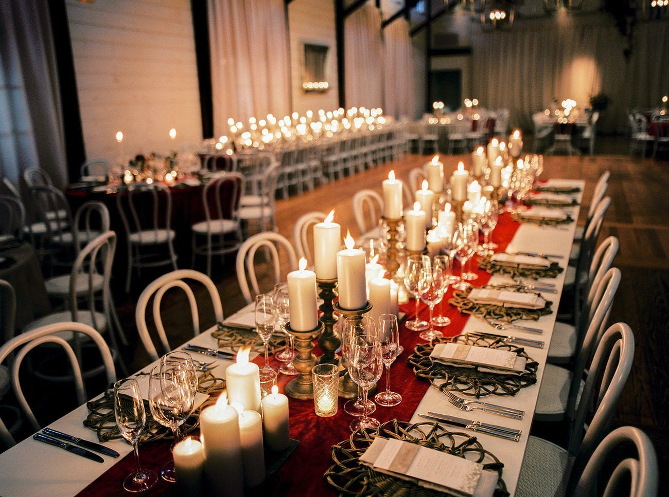 Rustic wedding reception table with candlelight and crimson table runner.