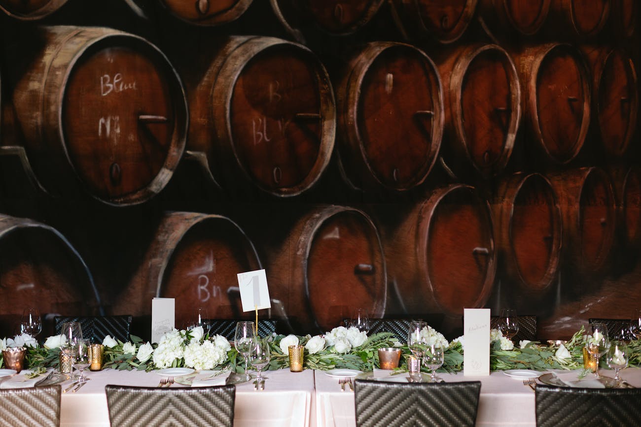 Wedding reception table against a backdrop of wine barrels | PartySlate