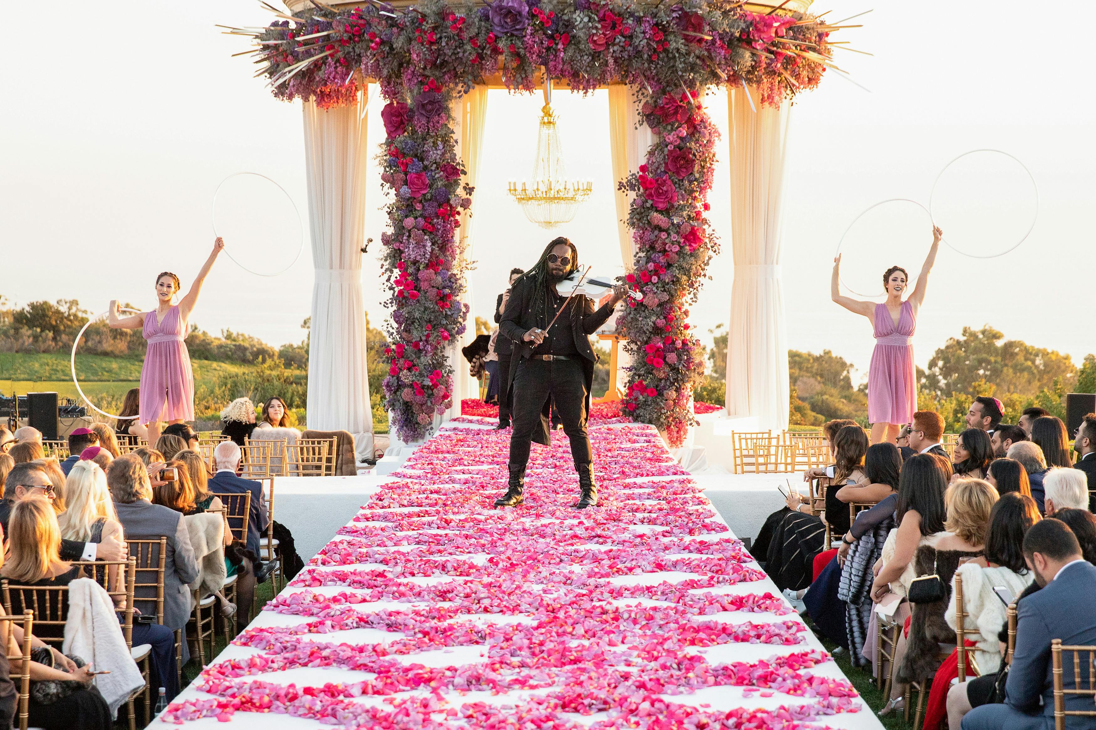 Unique Wedding Idea Where Man Plays Violin in Middle of Pink Petal-Strewn Wedding Aisle | PartySlate