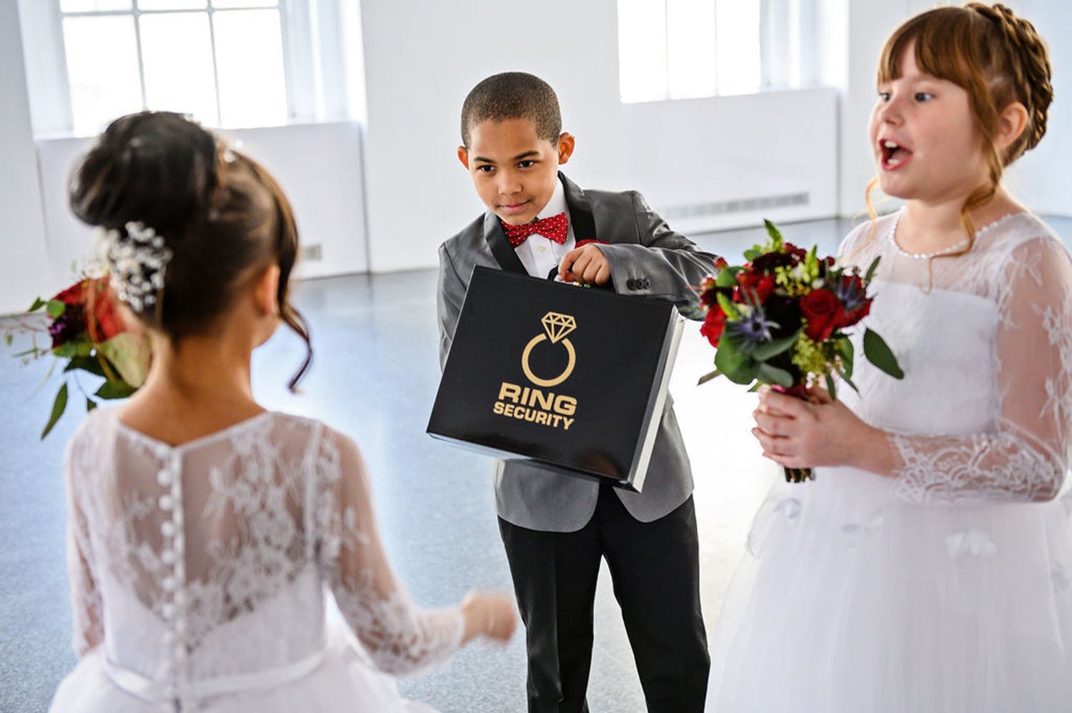 The ring bearer shows off his ring security box to flower girls | PartySlate