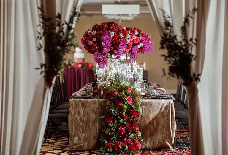 Photo of wedding table with pink orchid centerpieces and overflowing roses and greenery.