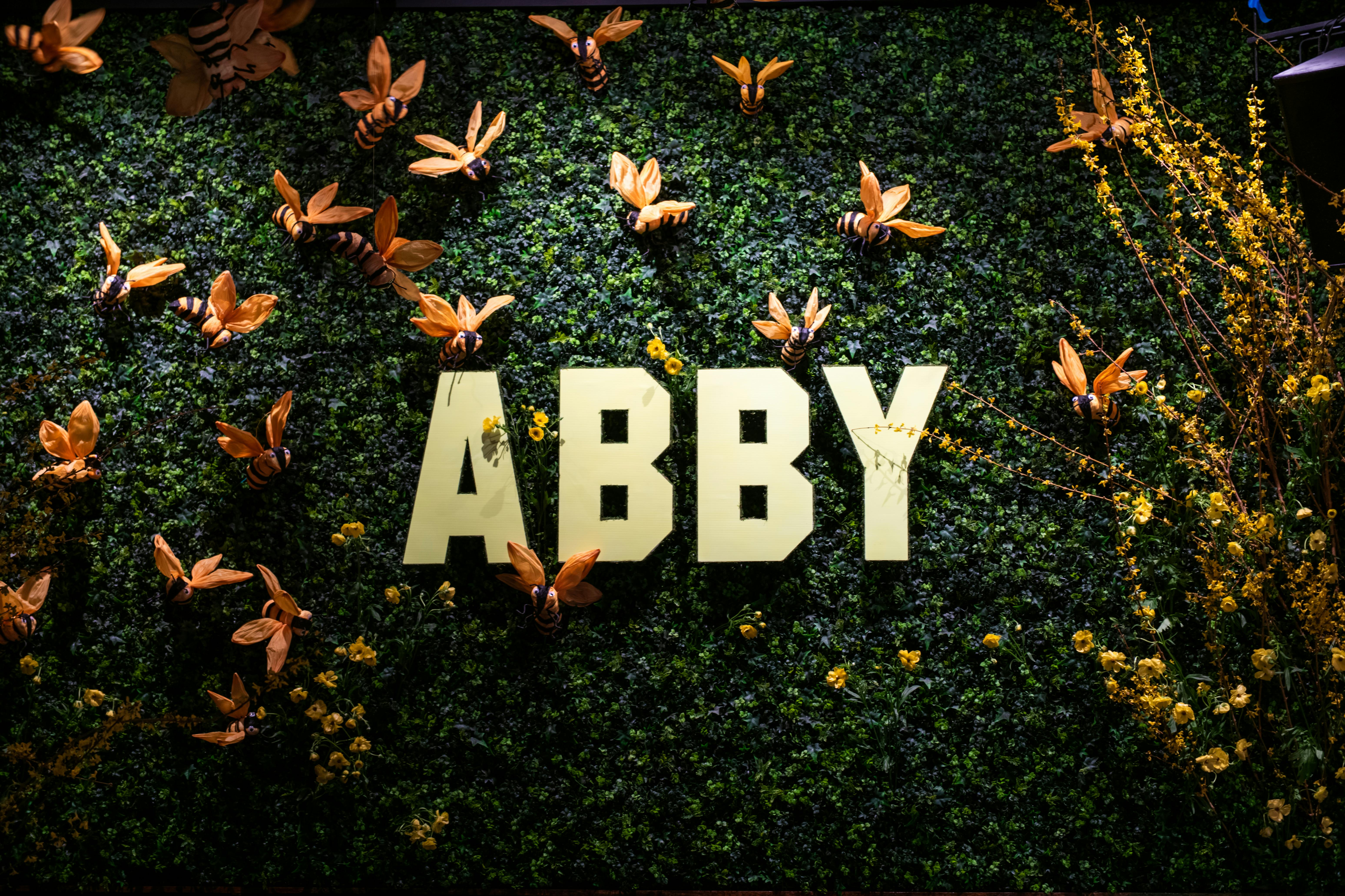 greenery wall with gold lettering and paper bees for photo op | PartySlate